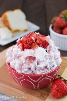 a bowl filled with whipped cream and strawberries on top of a wooden cutting board