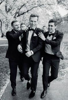 three men in tuxedos are walking down the sidewalk and one is holding his arm around another man's neck