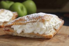 two pastries on a cutting board with apples in the background