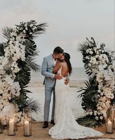 a bride and groom kissing in front of their wedding arch with candles on the beach