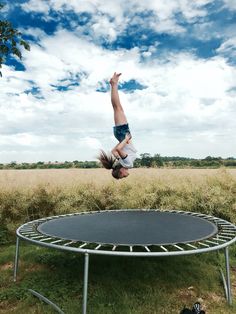 a person jumping in the air over a trampoline on a grassy field under a blue sky with white clouds