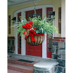 a hanging planter filled with greenery on the front steps of a house that is decorated for christmas