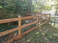 a wooden fence in the middle of a grassy area with trees and bushes behind it