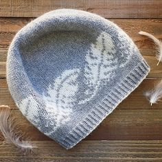 a knitted hat sitting on top of a wooden table next to feather quills