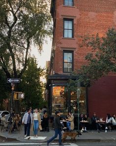 people are walking across the street in front of a brick building