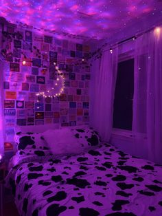 a bed with black and white bedspread covered in purple lights next to a window