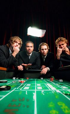 four men in suits sitting at a roule table with casino chips on the table