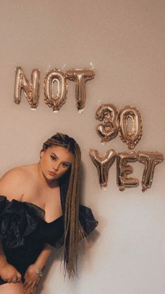 a woman leaning against a wall with balloons in the shape of words not so yet