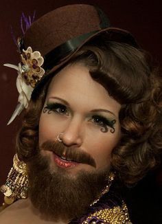 a man with a beard wearing a top hat and gold jewelry is posing for the camera