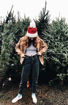 a woman wearing a red and white knitted hat standing in front of a christmas tree