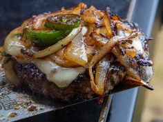 a hamburger with onions, cheese and pickles on it sitting on top of a grill