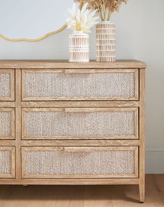 two vases on top of a wooden dresser with wicker drawers and roped handles