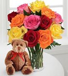 a teddy bear sitting next to a vase filled with multicolored roses