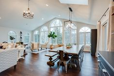 a large open concept living and dining room area with wood floors, high vaulted ceilings, white walls, and arched windows