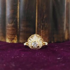 a yellow gold ring with a diamond center sits on a purple velvet surface in front of bookshelves