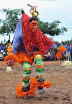 a woman in an orange and green outfit is dancing with feathers on her feet while people watch from the sidelines