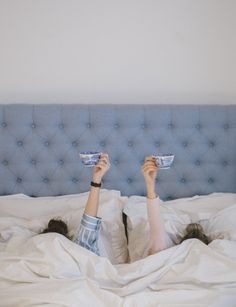 a woman laying in bed with her feet up on the pillow and holding a cup