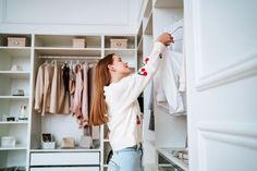 a woman is hanging clothes on a rail in a closet with white cabinets and drawers