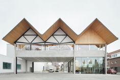 the building has three triangular roof tops on it's sides and two cars parked in front