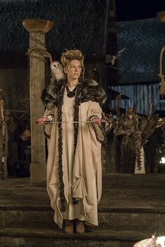 a woman dressed in medieval clothing standing on steps with candles lit up behind her and other people around her