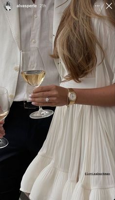 two people holding wine glasses with white wine in their hands and one person wearing a watch