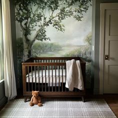 a baby crib with a teddy bear sitting in front of it and a painting on the wall