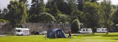 people are camping in the grass next to some parked cars and motorhome trailers