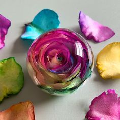 multicolored flowers are in a glass vase on a white surface with petals scattered around it