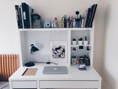 a white desk topped with a laptop computer next to a book shelf filled with books