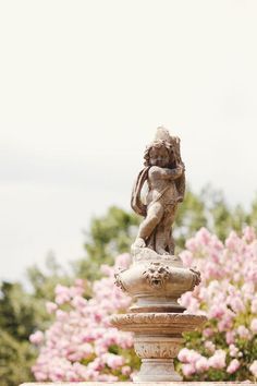 a statue is sitting on top of a stone pillar in front of some pink flowers