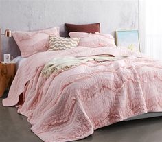 a bed with pink comforter and pillows in a room next to a painting on the wall