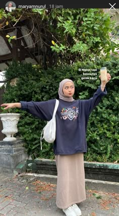 a woman standing in front of a bush holding a cup and wearing a hijab