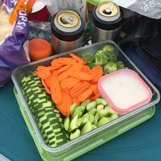 a container filled with vegetables next to two cans of sodas and other food items