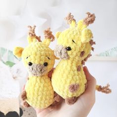 two crocheted giraffes are held in their hands