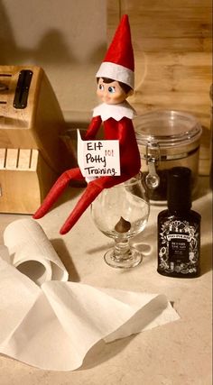 an elf sitting on top of a counter next to a roll of toilet paper and a bottle