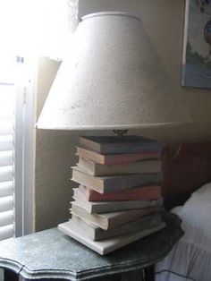 a lamp sitting on top of a table next to a pile of books in front of a window