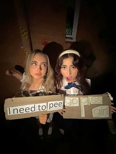 two girls dressed in costumes holding up a cardboard sign that says need to pee, piss girl