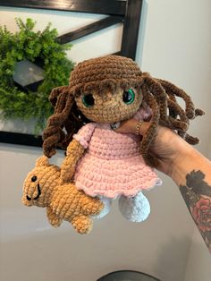 a hand holding a small crocheted doll with a teddy bear attached to it