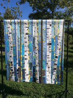 a quilt is hanging on a stand in the grass near some trees and green grass