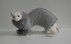 a stuffed animal with a sweater on it's head and tail is standing in front of a gray background