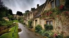 an old stone house with flowers growing on the windows and in the street next to it