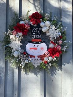 a wreath with a snowman on it and christmas decorations around the wreath is hanging on a wooden fence