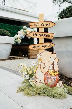 a winnie the pooh wooden sign with flowers in front of it that says, welcome hundreds after wood