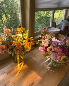 two vases filled with colorful flowers sitting on a wooden table next to a window