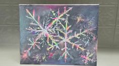 a snowflake is painted on a black board with multicolored paint sprinkles