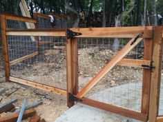 a wooden gate with wire around it on top of a dirt ground next to trees