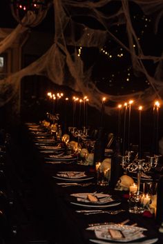 a long table is set with candles and plates in the dark for a halloween party