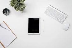 an overhead view of a tablet, keyboard and mouse on a white desk with a notepad