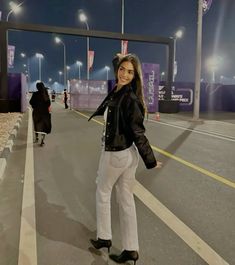 a woman standing in the middle of an empty street at night with her arms outstretched