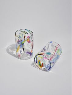 two glass cups sitting next to each other on top of a white surface with colorful designs